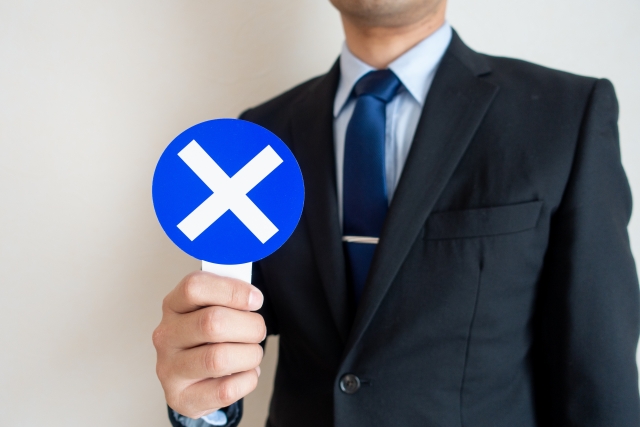 ×を出す男性の写真